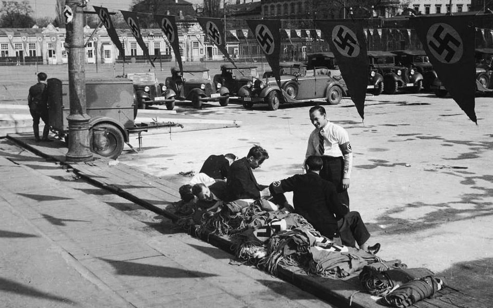 Austria, Vienna Young men sitting on a pile of swastika flags, army vehicles in the background 1938