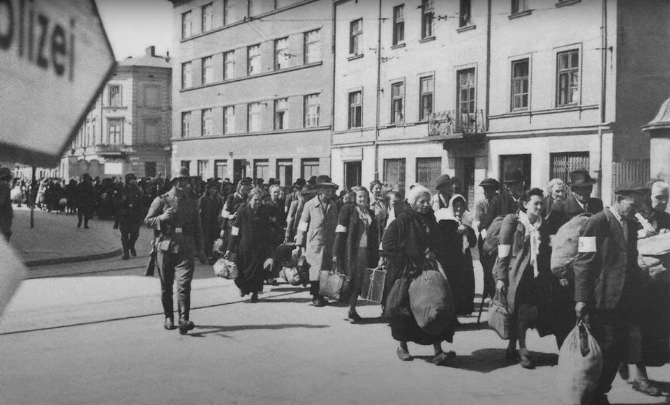 A column of captive Jews march with bundles down the main thoroughfare in Krakow during the liquidation of the Krakow Ghetto. SS guards oversee the deportation action to the extermination camps
