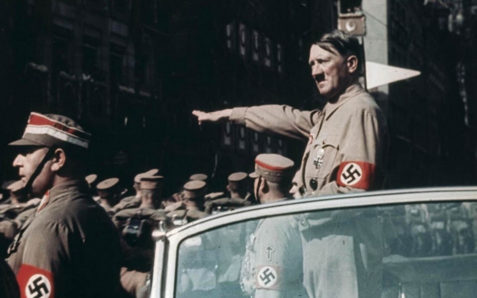 Hitler, wearing the uniform of the Sturm Abteilung (SA), salutes from an open topped car at Nuremberg on Party Day, September 1938