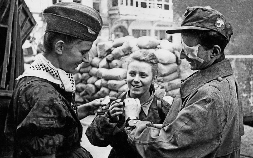 Female fighters chat and share a cigarette with a wounded comrade in Werecka Street, north Šródmieście district.