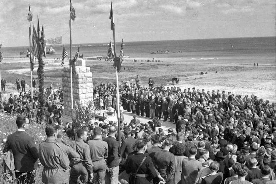 Crowd of civilians and military personnel gathered in 1945 in Saint-Laurent-sur-Mer, around the monument to the memory of American soldiers erected in front of Omaha Beach,